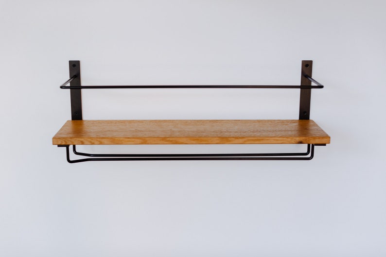 K&ouml;nnte beinhalten: Ein Holzregal mit einem schwarzen Metallrahmen und zwei schwarzen Metallstangen darunter. Das Regal ist an einer wei&szlig;en Wand montiert.