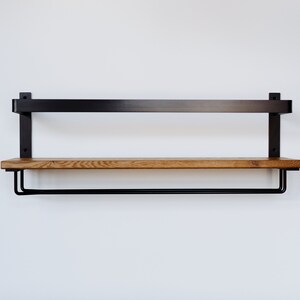May include: A black metal shelf with a wooden top and a metal rod underneath. The shelf is mounted to a white wall.