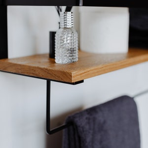 May include: A black metal shelf with a wooden top, a clear glass bottle with a silver cap, and a black towel hanging from a metal hook.