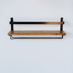 May include: A black metal shelf with a wooden top and a metal bar underneath. The shelf is mounted to a white wall.