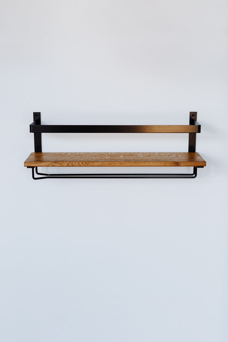 May include: A black metal shelf with a wooden top and a metal bar underneath. The shelf is mounted to a white wall.