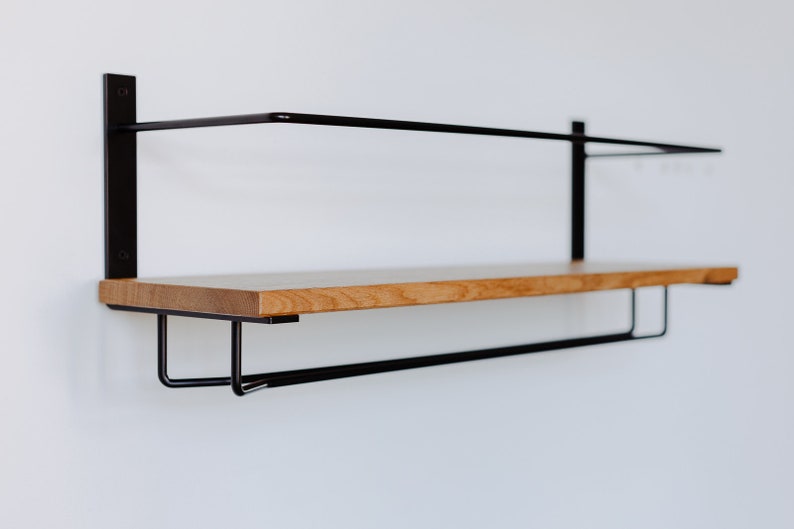 K&ouml;nnte beinhalten: Ein schwarzes Wandregal aus Metall mit einer Holz-Oberplatte und einer Metallstange darunter. Das Regal ist an einer wei&szlig;en Wand montiert.
