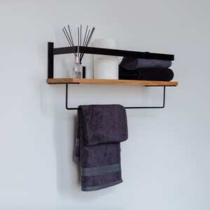 May include: A black metal shelf with a wooden top, featuring a towel bar and a towel hanging from it. The shelf is decorated with a diffuser, candles, and folded towels.