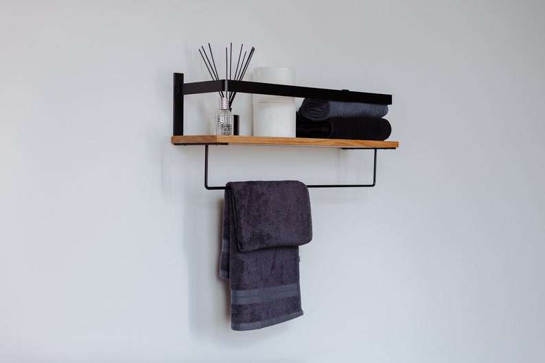 May include: A black metal shelf with a wooden top, featuring a towel bar and a towel hanging from it. The shelf is decorated with a diffuser, candles, and folded towels.