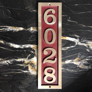 May include: A vertical house number plaque with a burgundy background and gold numbers. The numbers are 6028.