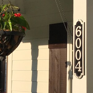 May include: A black and white house number sign with the number 6004 on it. The sign is mounted on a white column.