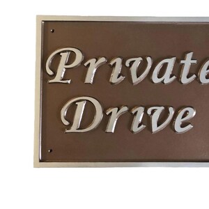 以下が含まれることがあります： 茶色の背景に銀色の文字で「Private Drive」と書かれた銀色のプレートです。