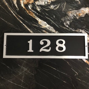 May include: A silver rectangular house number plaque with a black background and the number 128 in white.