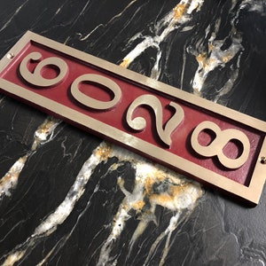 May include: A rectangular brass house number plaque with a red background. The numbers "8028" are cut out of the brass and are raised against the red background.