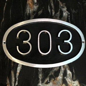May include: A silver oval-shaped house number plaque with a black background and the number 303 in white.