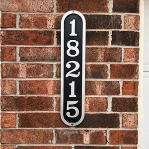 May include: A black and silver vertical house number sign with the number 18215 printed in white.