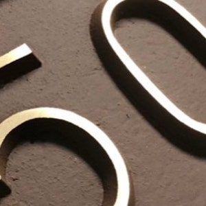May include: Close-up of a gold-colored metal number "50" on a brown background.