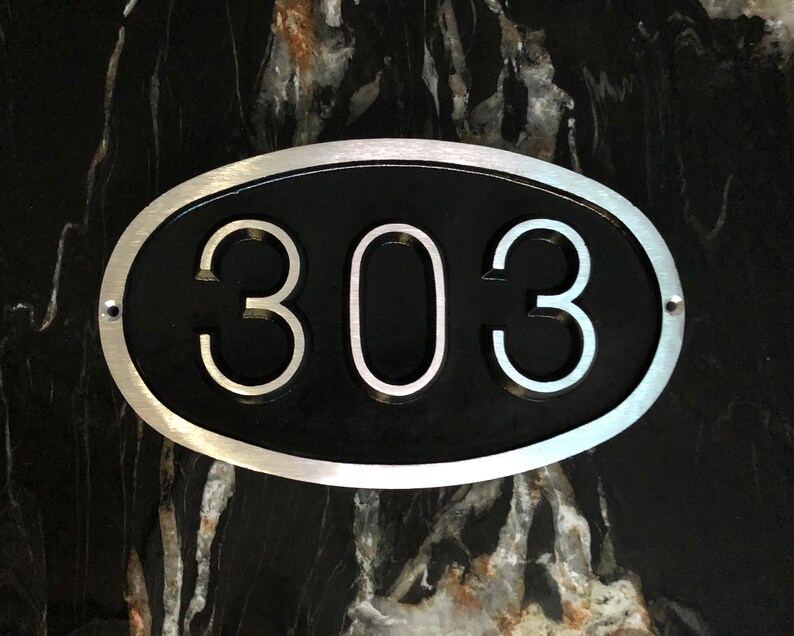 May include: A silver oval-shaped house number plaque with a black background and the number 303 in white.
