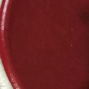 May include: A close-up of a deep red, smooth, circular surface. The surface appears to be a painted or coated material.