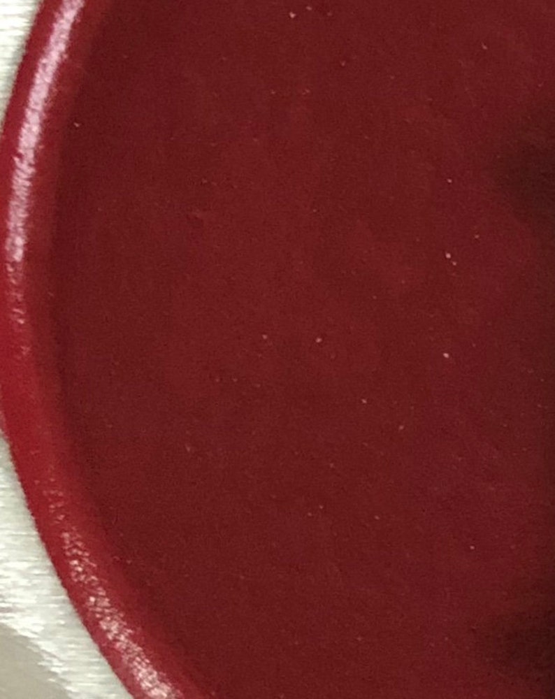 May include: A close-up of a deep red, smooth, circular surface. The surface appears to be a painted or coated material.