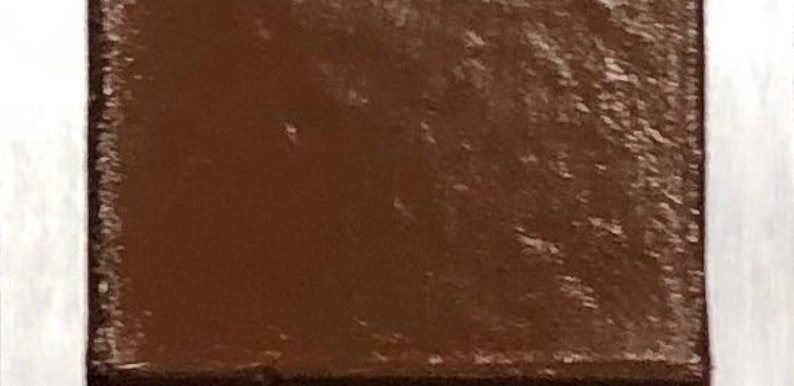 May include: A close-up of a small, square, brown tile with a textured surface.