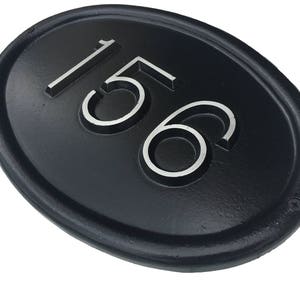 May include: Black oval-shaped house number plaque with the number 156 in white raised lettering.
