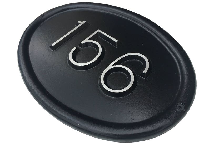 May include: Black oval-shaped house number plaque with the number 156 in white raised lettering.
