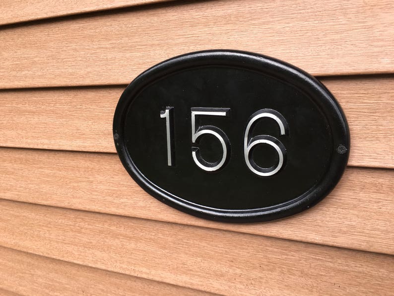 May include: A black oval-shaped house number plaque with a white background and the number 156 in silver lettering.