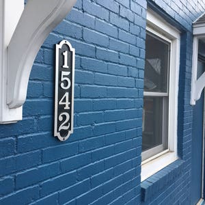 May include: A blue brick building with a white awning and a silver house number plaque that reads "1542".