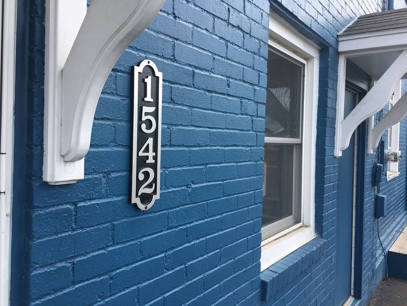 May include: A blue brick building with a white awning and a silver house number plaque that reads "1542".