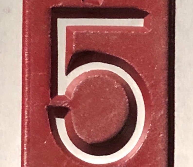 May include: A close-up of a red number five with a white outline. The number is raised and has a textured surface.