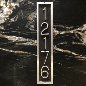 May include: A silver metal house number plaque with the numbers 12176 on a black background.