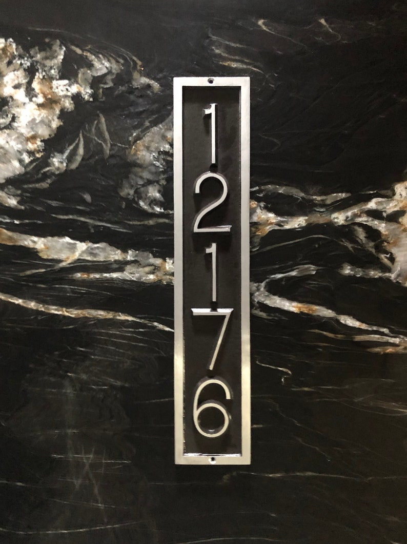 May include: A silver metal house number plaque with the numbers 12176 on a black background.
