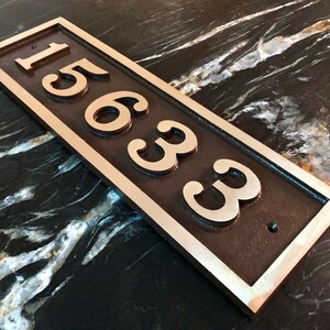 May include: A rectangular bronze house number plaque with a silver border. The number "15633" is engraved in a decorative font.
