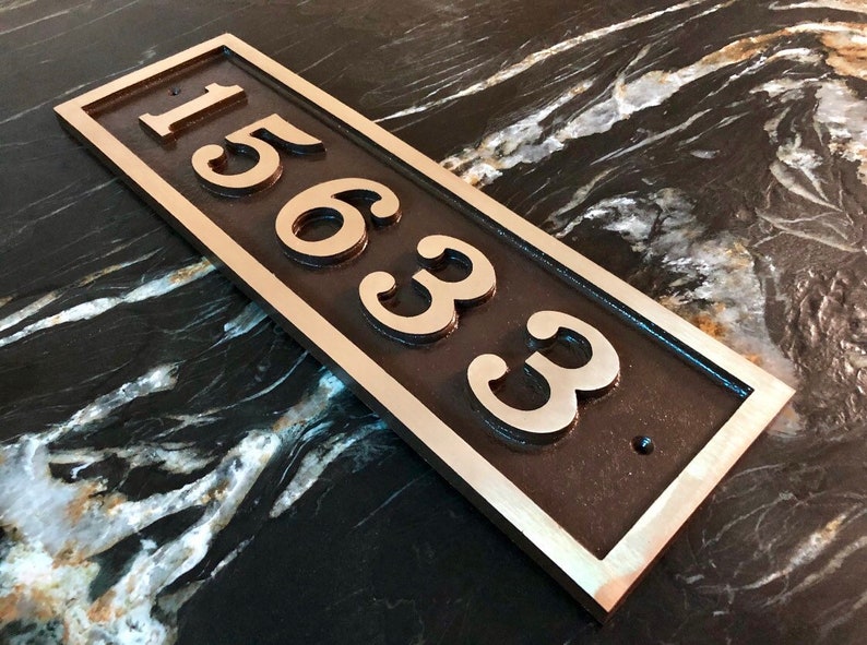 May include: A rectangular bronze house number plaque with a silver border. The number "15633" is engraved in a decorative font.