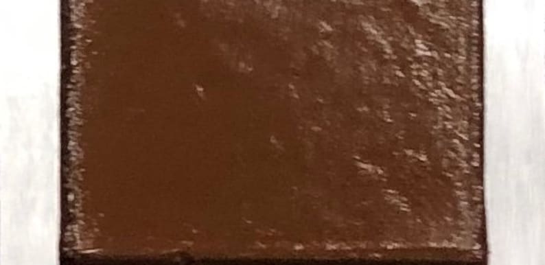 May include: A close-up of a small, square, brown tile with a textured surface.