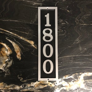 Puede incluir: Un letrero de n&uacute;mero de casa de metal plateado con fondo negro y n&uacute;meros blancos. El n&uacute;mero es 1800.