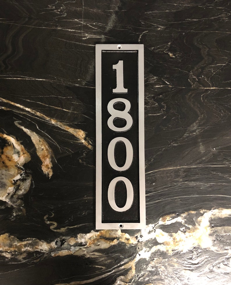 Puede incluir: Un letrero de n&uacute;mero de casa de metal plateado con fondo negro y n&uacute;meros blancos. El n&uacute;mero es 1800.