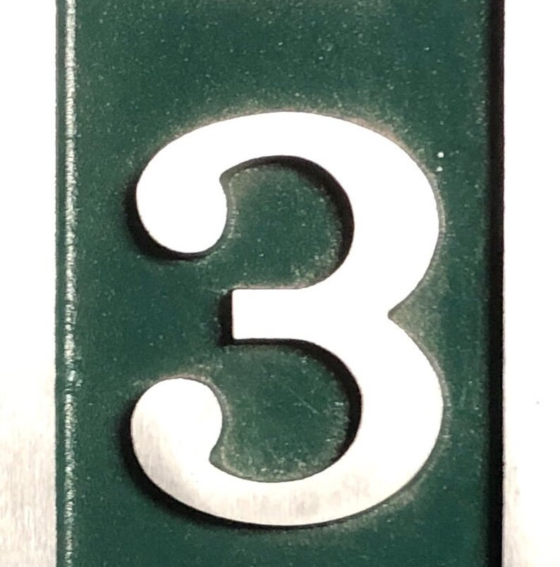Puede incluir: Un n&uacute;mero tres blanco sobre un fondo verde oscuro. El n&uacute;mero est&aacute; recortado del fondo y est&aacute; en relieve.