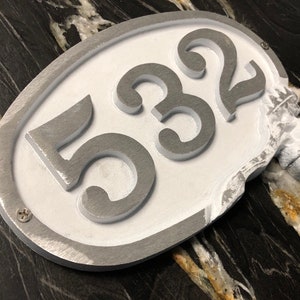 May include: A white oval-shaped house number sign with silver raised numbers "532" and a decorative acorn on the side.