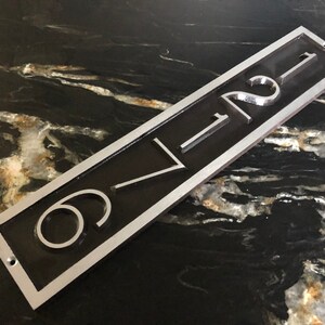 May include: A silver and black metal house number plaque with the number "621" engraved in white.