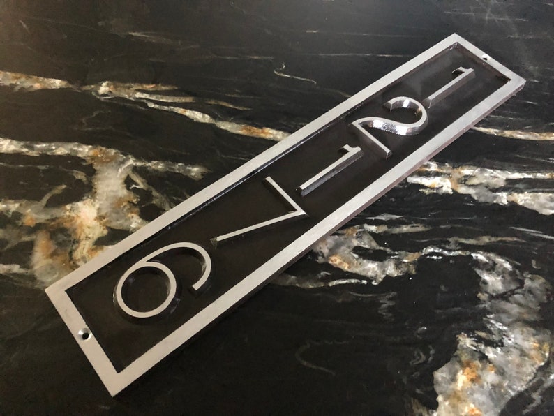 May include: A silver and black metal house number plaque with the number "621" engraved in white.