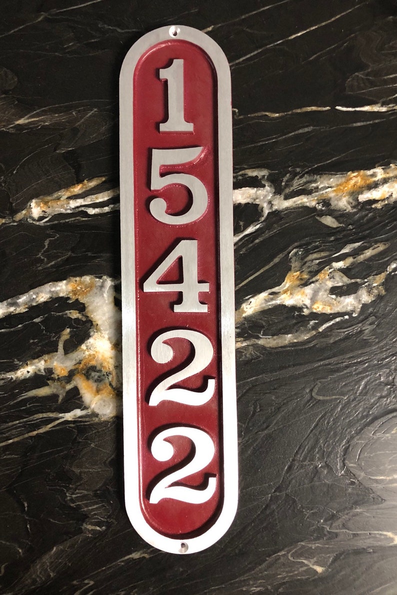 May include: A vertical, oval-shaped house number sign with the numbers 15422 in silver on a burgundy background.