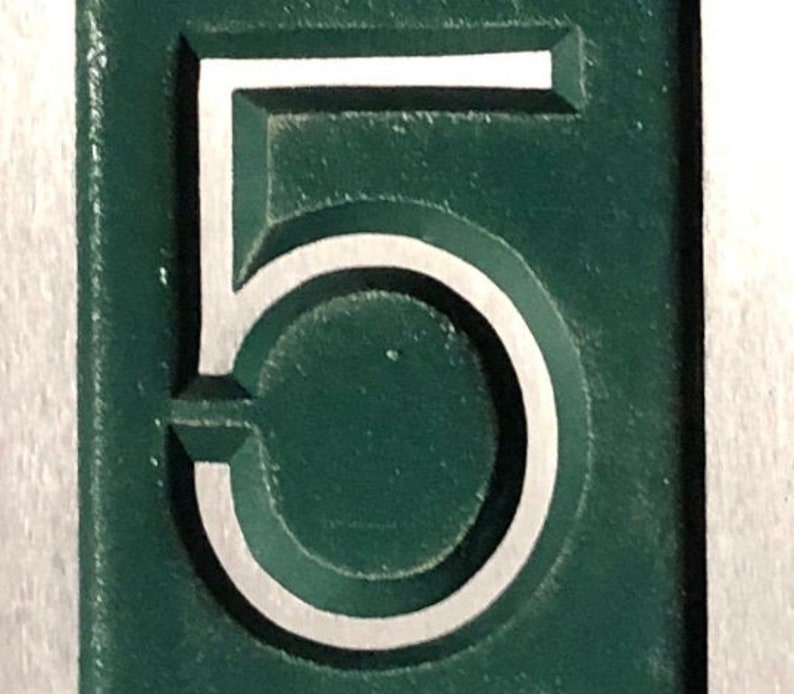 May include: A close-up of a green metal plaque with the number "5" embossed in white.