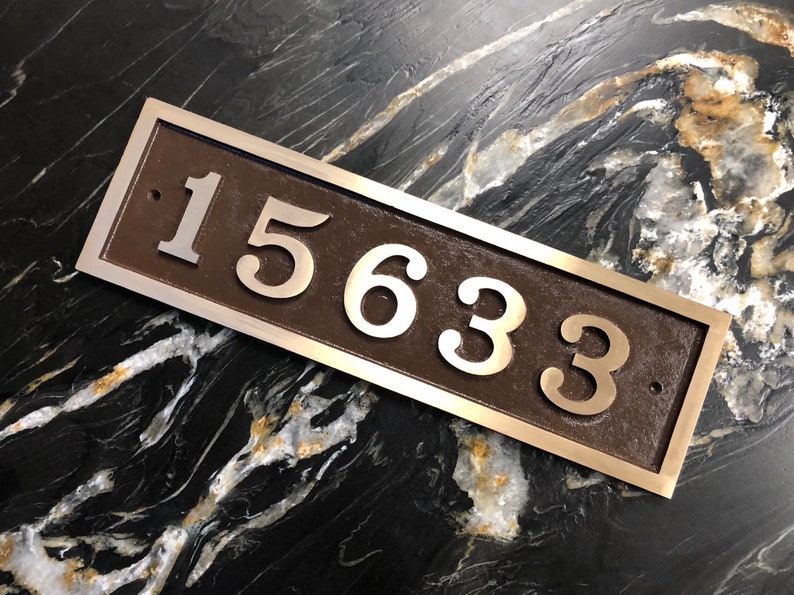 May include: A rectangular house number plaque with a brown background and silver raised numbers. The numbers are 15633.