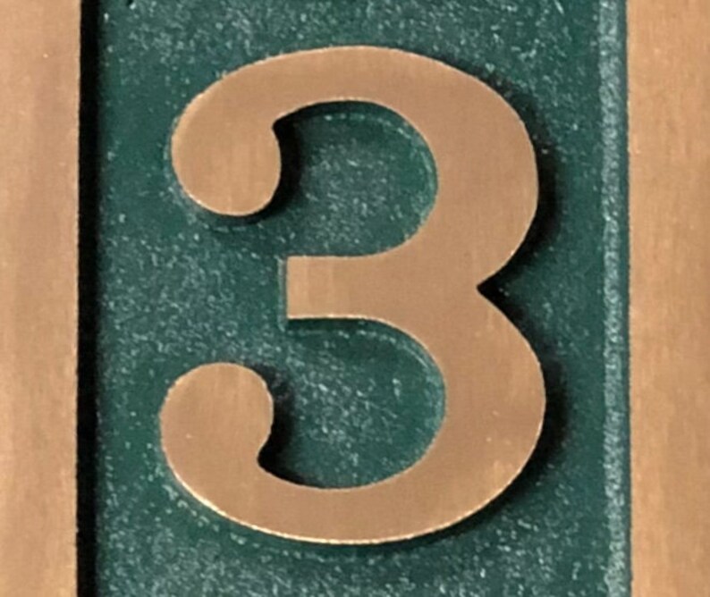 May include: A close-up of a copper-coloured number "3" on a green background. The number is raised and has a textured surface.
