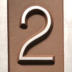 May include: A close-up of a silver number "2" embossed on a brown background.