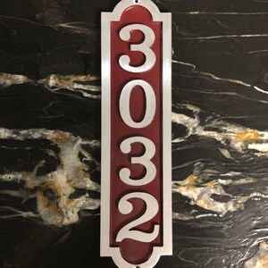 May include: A vertical silver house number sign with a red background. The number 3032 is displayed in white on the sign.
