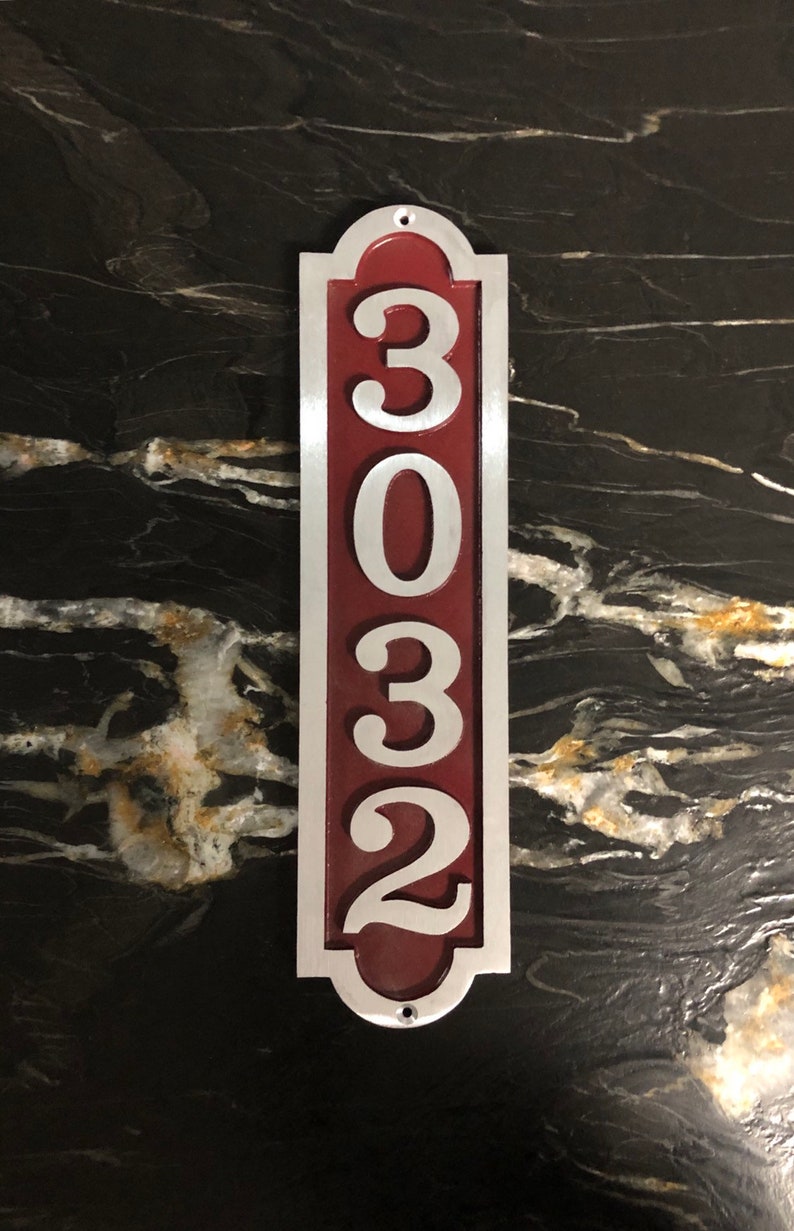 May include: A vertical silver house number sign with a red background. The number 3032 is displayed in white on the sign.