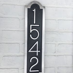 May include: A vertical silver and black house number sign with the numbers 1542 in white.