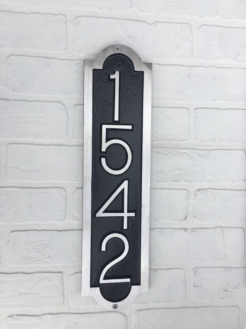 May include: A vertical silver and black house number sign with the numbers 1542 in white.