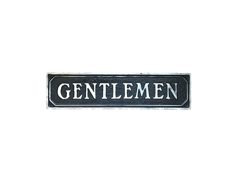May include: A black rectangular sign with a silver border and the word "GENTLEMEN" in white lettering.