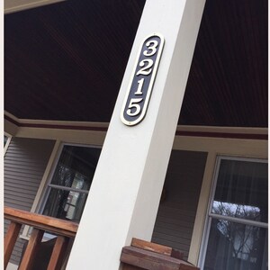 May include: A white wooden porch post with a black and gold house number plaque that reads "3215".