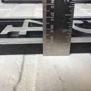 May include: Close-up of a black and silver metal house number plaque with the number "04" visible. A ruler is placed next to the plaque to show the size.