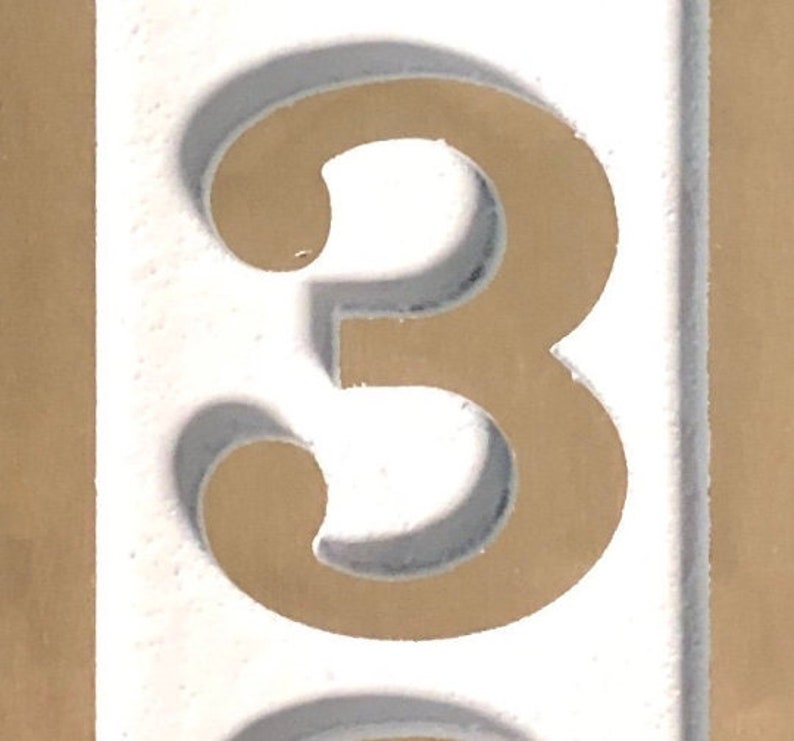 May include: A white background with a gold number three. The number is raised and has a shadow.